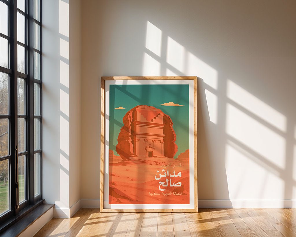 The FN Prints "Qasr al-Farid Madain Saleh" framed poster, with Arabic text and a monument illustration, rests on a wooden floor by a beige wall as sunlight streams in, casting soft shadows.