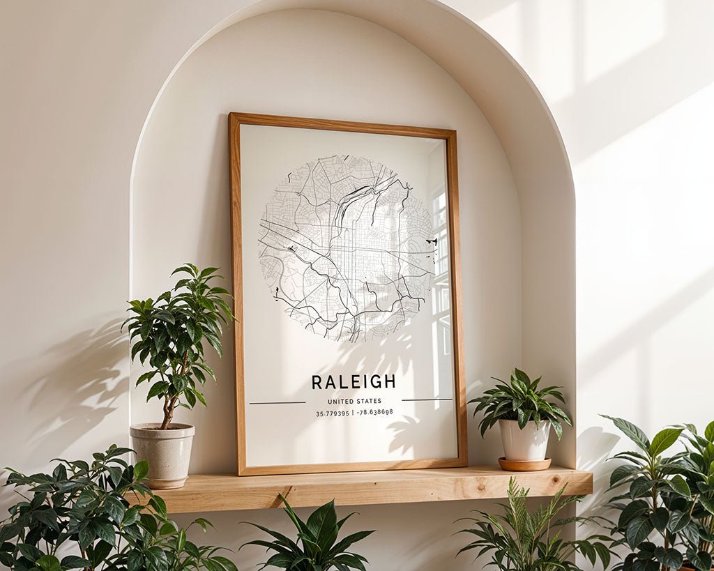 The Raleigh City Map by FN Prints features a minimalist design. It's framed on a wooden shelf within a white arched alcove alongside three potted plants. Crafted with eco-friendly inks, sunlight gracefully casts shadows, enhancing its serene ambiance.