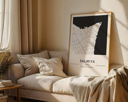 A framed FN Prints Salmiya City Map on museum-quality fine art paper rests against a light beige sofa with cushions. A cream-colored throw blanket adorns the sofa arm, while sunlight streaming through a window casts soothing shadows on this serene setting.