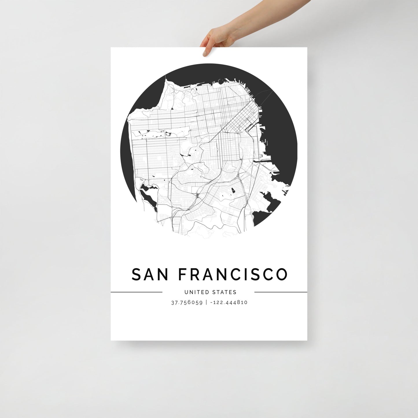 A hand holds a minimalist FN Prints' "San Francisco City Map," displaying streets and lines. Beneath, it reads "San Francisco, United States" with coordinates "37.756959 | -122.444810." Ideal for modern interiors.