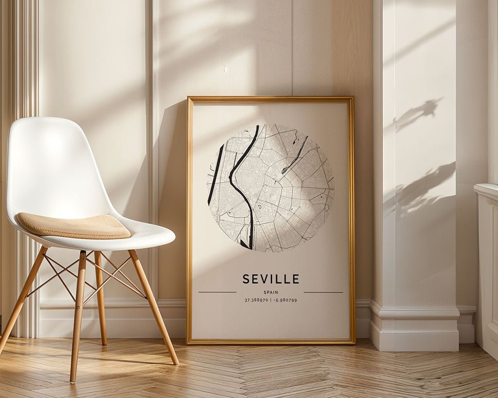 FN Prints' Seville City Map, an elegant black and white framed poster with minimal black lines on a white background, leans against a wall in a sunlit room. Nearby, a white chair with a cushion highlights the light herringbone pattern of the wooden floor.