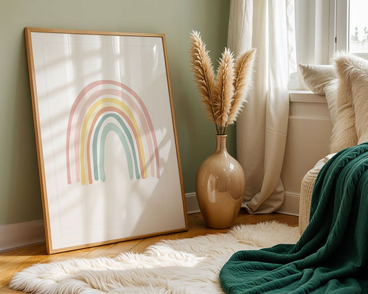 FN Prints' Soft Rainbow framed art print is propped against a light green wall. A beige vase with pampas grass embodies minimalist design. A white fluffy rug and a chair draped with a green blanket create a cozy corner near a window adorned with sheer curtains.