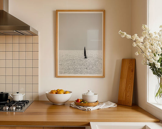 A modern kitchen with a wooden countertop, stove, bowl of oranges, white teapot and cups, vase of white flowers, and FN Prints’ “Solo Sail” framed sailing boat wall art decorates the wall.