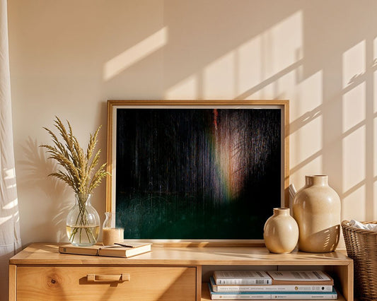 The framed "Spectrum" abstract artwork by FN Prints, featuring dark colors and a hint of rainbow, sits on a wooden cabinet with ceramic vases, a glass jar of dried wheat, and books about Chouf Lebanon bathed in sunlight.