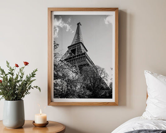 The Eiffel Tower: Part II" by FN Prints, a framed black and white Paris wall art, hangs above a bed with a bedside table featuring a potted plant, lit candle, and small dish.
