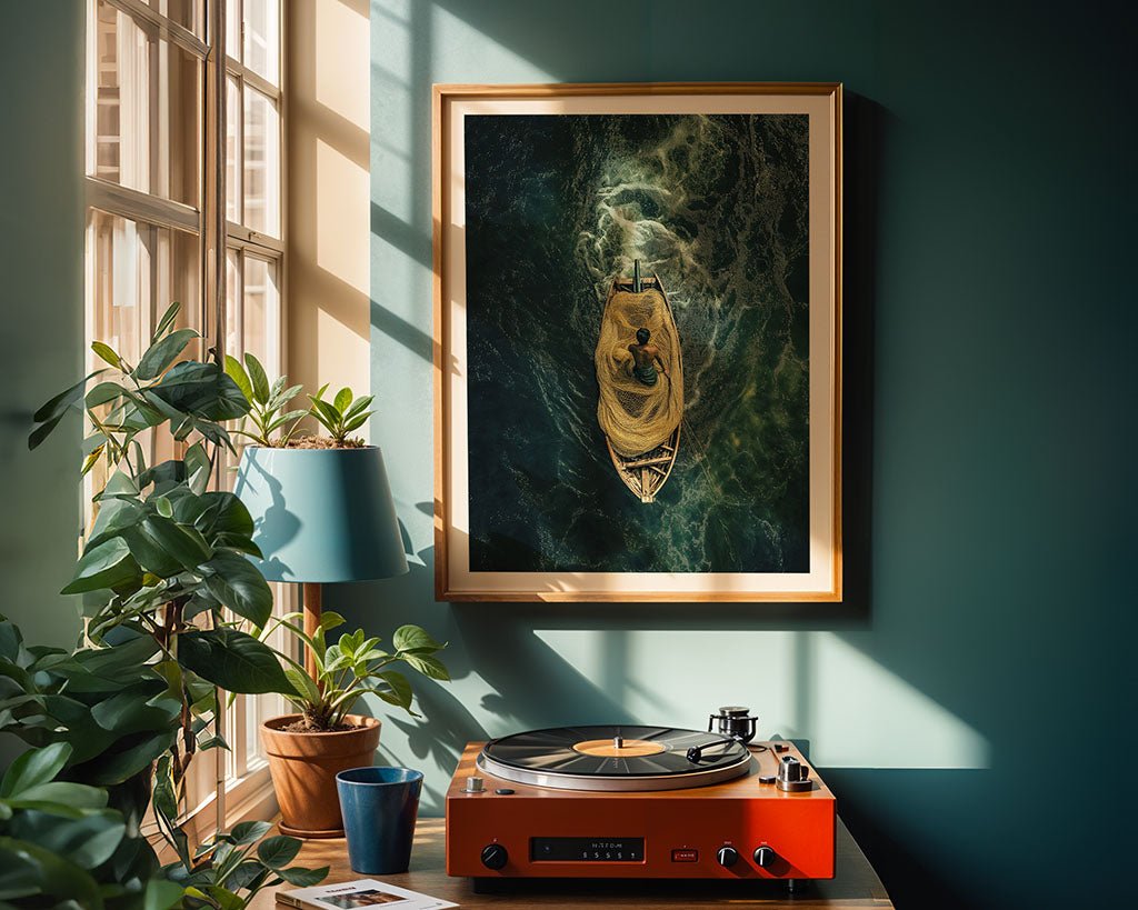 A cozy room with sunlit windows showcases FN Prints' "The Fisherman" artwork, highlighting the bond between man and nature on a green sea. Below is a red turntable beside a potted plant and a blue lamp, adding to the coastal-themed decor against teal walls.