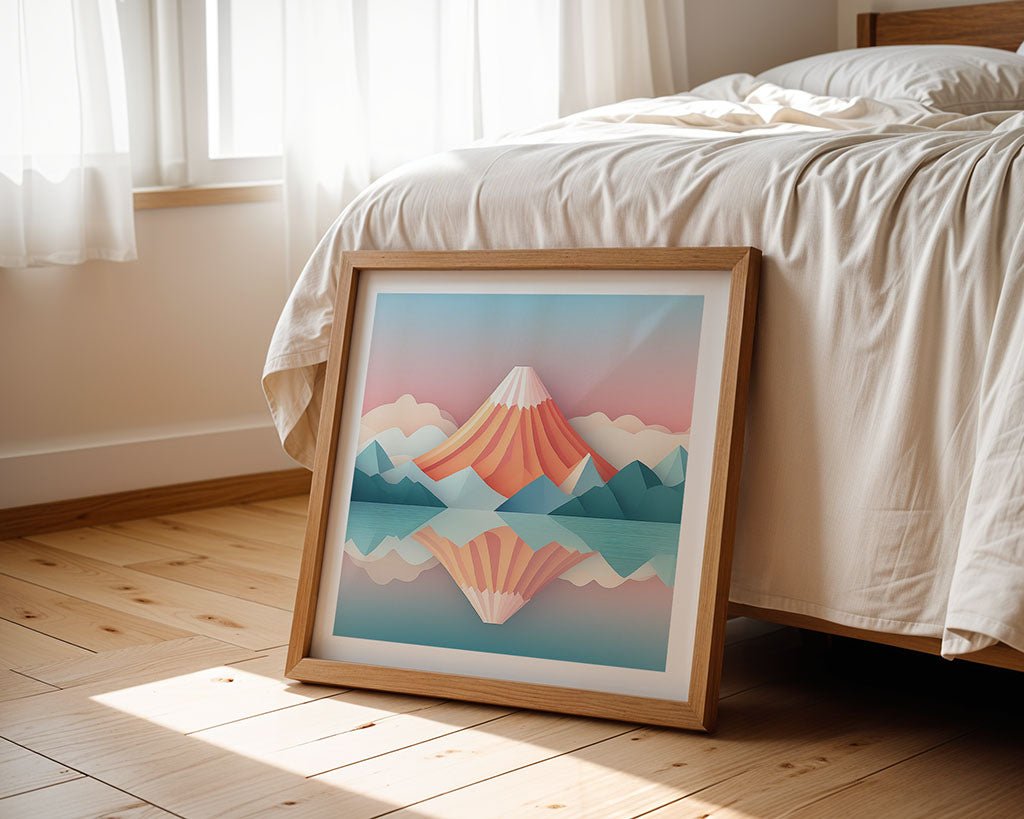 The Perfect Reflection by FN Prints, a framed digital artwork featuring a stylized mountain and lake reflection with a unique folded paper effect, is displayed against a bed. The room boasts wooden flooring and sheer curtains that allow natural light to filter in. The bed is neatly made with white sheets.
