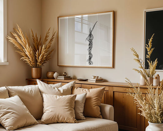 A cozy living room features a beige sofa with matching pillows. Behind it, a wooden sideboard displays decorative items and vases with dried pampas grass. FN Prints' "The Serpentine Cross Sculpture: Mount Nebo, Jordan" black-and-white photograph graces the wall, bathed in natural light.