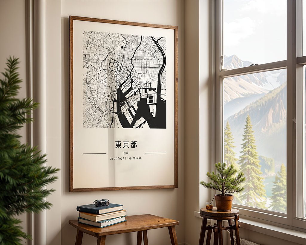A framed FN Prints Tokyo City Map hangs on a wall beside a window with mountain views. Below the minimalist black-and-white art, a small table holds stacked books, a camera, and a potted plant.