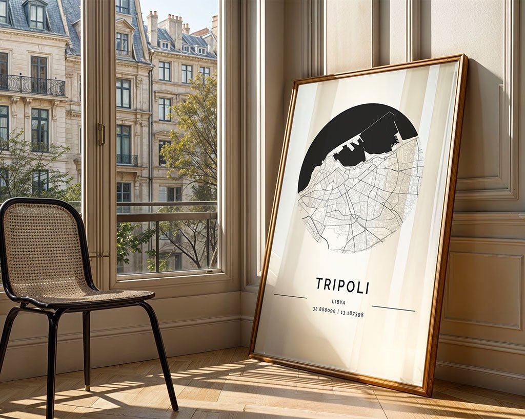 A Tripoli City Map by FN Prints, displaying urban details and coordinates, leans against a wall on the wooden floor. Nearby, an empty wicker chair complements the scene, with large windows revealing classic European-style buildings and trees outside.