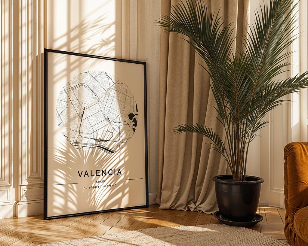An FN Prints framed Valencia City Map leans stylishly against the wall on a wooden floor, complementing the décor. Sunlight filters through a nearby potted palm, casting shadows on the minimalist print, while curtain fabric and an orange chair add to the room's warm tones.