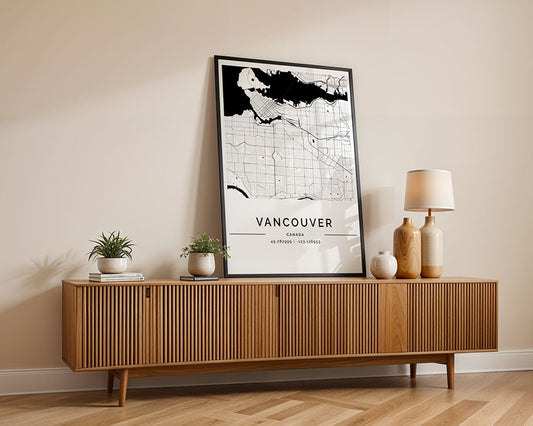 A wooden sideboard with a ribbed texture sits against a beige wall, adorned with the FN Prints Vancouver City Map poster. Two small potted plants and a lamp with a beige shade perfect this stylish arrangement.
