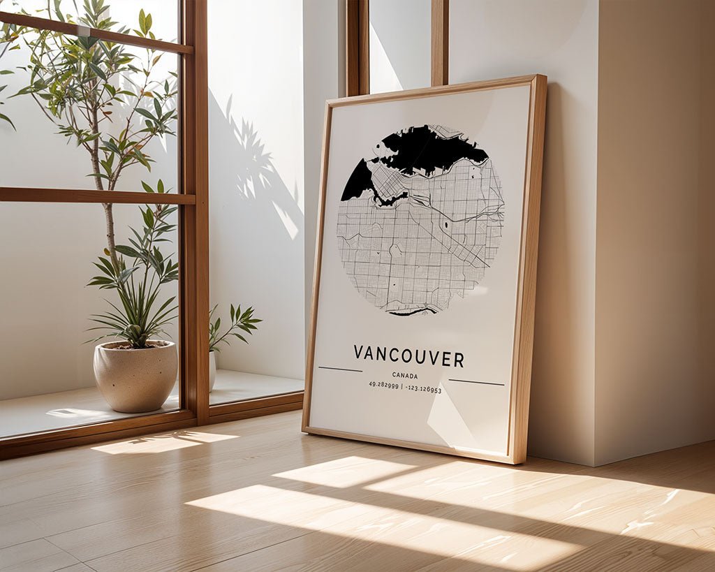 A FN Prints Vancouver City Map poster with coordinates leans elegantly against a sunlit surface, complemented by a potted plant on the wooden floor, adding warmth and charm to the serene setting.
