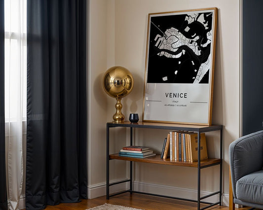 A small room features a FN Prints Venice City Map on a console table with a modern golden lamp and some books, partially in natural light from a black curtain-draped window. A grey armchair is slightly visible, enhancing the serene ambiance.