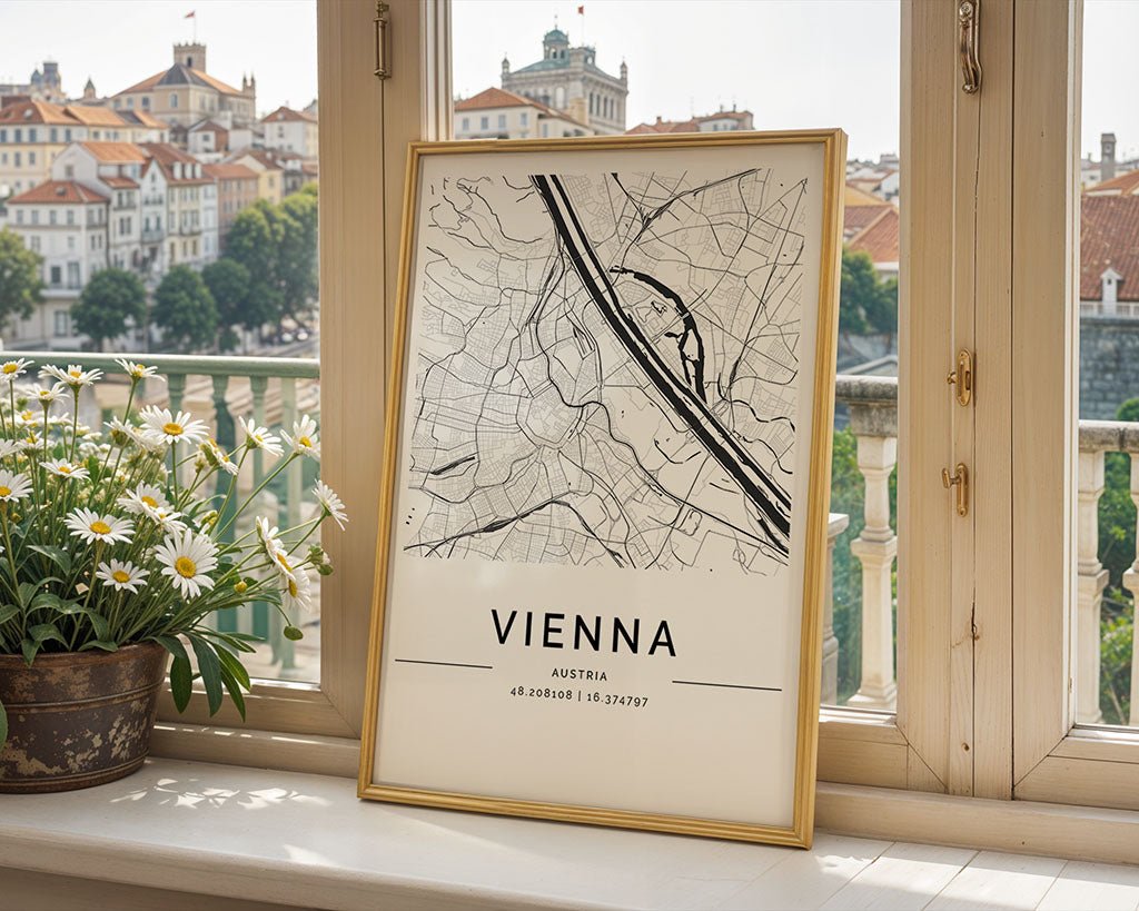 A framed Vienna City Map by FN Prints rests on the windowsill, showcasing its coordinates elegantly. Outside, classic European architecture complements the scene. A potted plant with daisy-like flowers adds nature's touch to this charming wall art print.