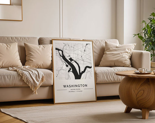 The Washington City Map by FN Prints leans against a beige sofa with neutral cushions and a light blanket. A round wooden coffee table and potted plant finish this bright, modern living room with minimalist map print style.