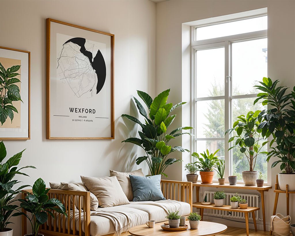 A cozy room with a light gray sofa, wooden frame, and cushions showcases minimalist design. Potted plants grace tables and the floor, while the FN Prints Wexford City Map adorns the wall. Light floods through a large window, enhancing the bright atmosphere.