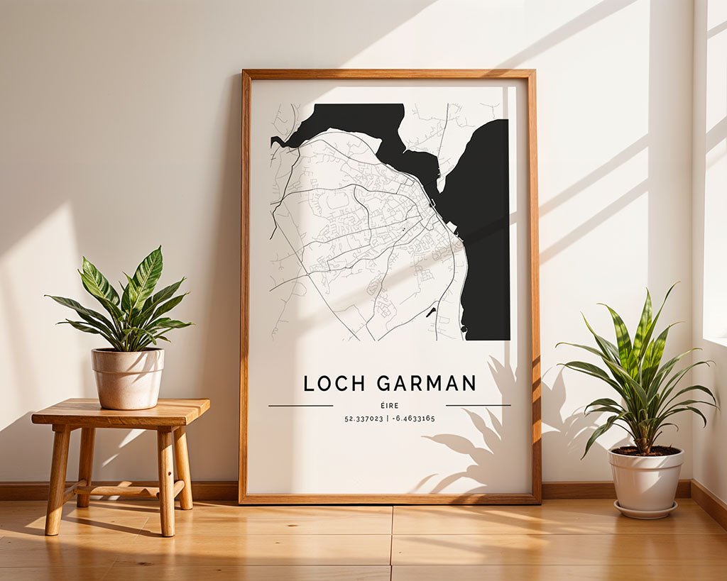 A framed FN Prints Wexford City Map, designed minimally, rests on the wooden floor against a wall. It is flanked by two potted plants, one on a small wooden stool. Sunlight highlights the high-quality print, casting artistic shadows around it.