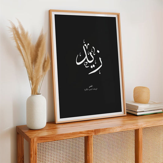 A framed black "Zaid - زيد" poster from FN Prints' Arabic Names Collection rests on a wooden console with pampas grass, books, and decor—creating a minimal, modern look perfect for Islamic wall art enthusiasts.