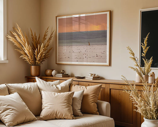 A beige living room features a cream sofa, dried pampas grass in vases, a wooden sideboard, and striking wall art—a large "Zanzibari Woman" FN Prints photograph. Natural light streams in from a nearby window.