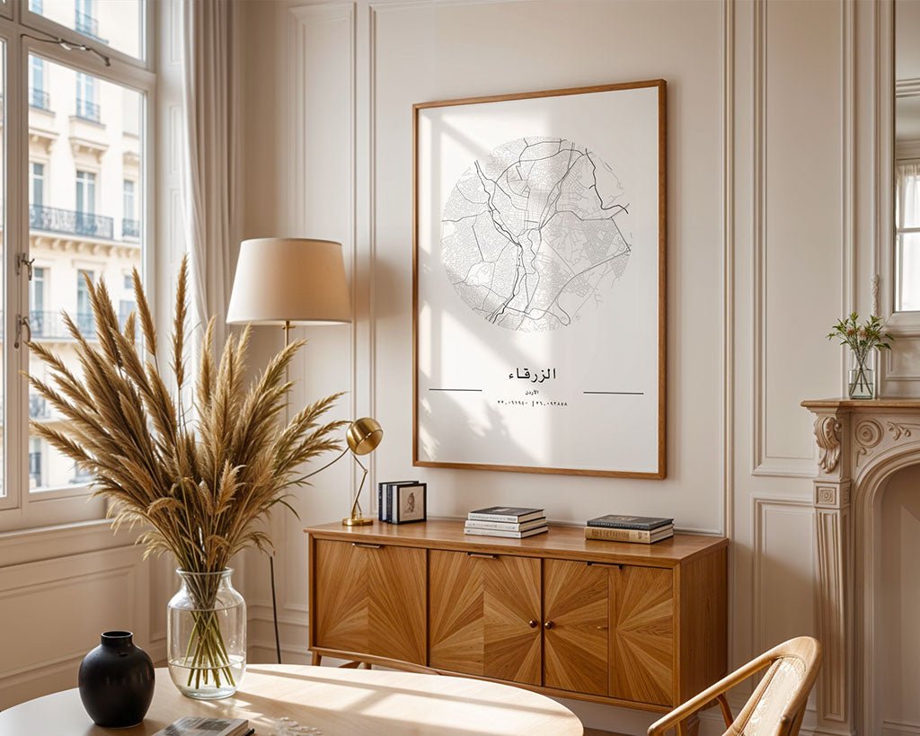 A bright living room features a stunning Zarqa City Map by FN Prints on the wall, with a wooden sideboard displaying books and a lamp. A round table sits gracefully as natural light highlights pampas grass in a vase, enhancing the room's warm and elegant minimalist décor.