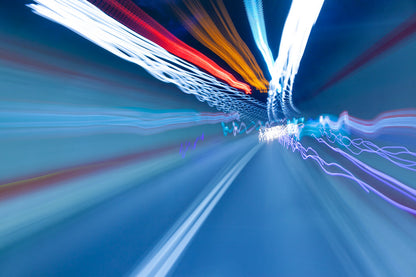 In this abstract photography piece by FN Prints, titled "Warp Speed," blurry and colorful light trails stretch through a tunnel, crafting a dynamic urban landscape with streaks of blue, red, yellow, and white that evoke motion or speed.