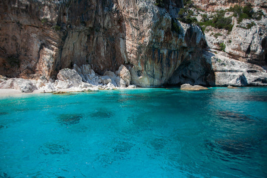 Experience the serenity and natural beauty with FN Prints' "Sardinian Coast: Part II." This captivating work features a stunning turquoise crystal sea surrounded by rugged rocky cliffs and a secluded sandy beach. The clear water unveils darker underwater formations, while sparse greenery lines the majestic Sardinian coastline.