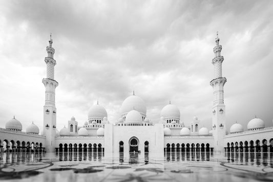 Black and white photography print of the Sheikh Zayed Grand Mosque, from FN Prints, capturing its grand architecture with multiple domes and tall minarets. The intricate floor reflects the mosque's solemn magnificence against a dramatic cloudy sky.