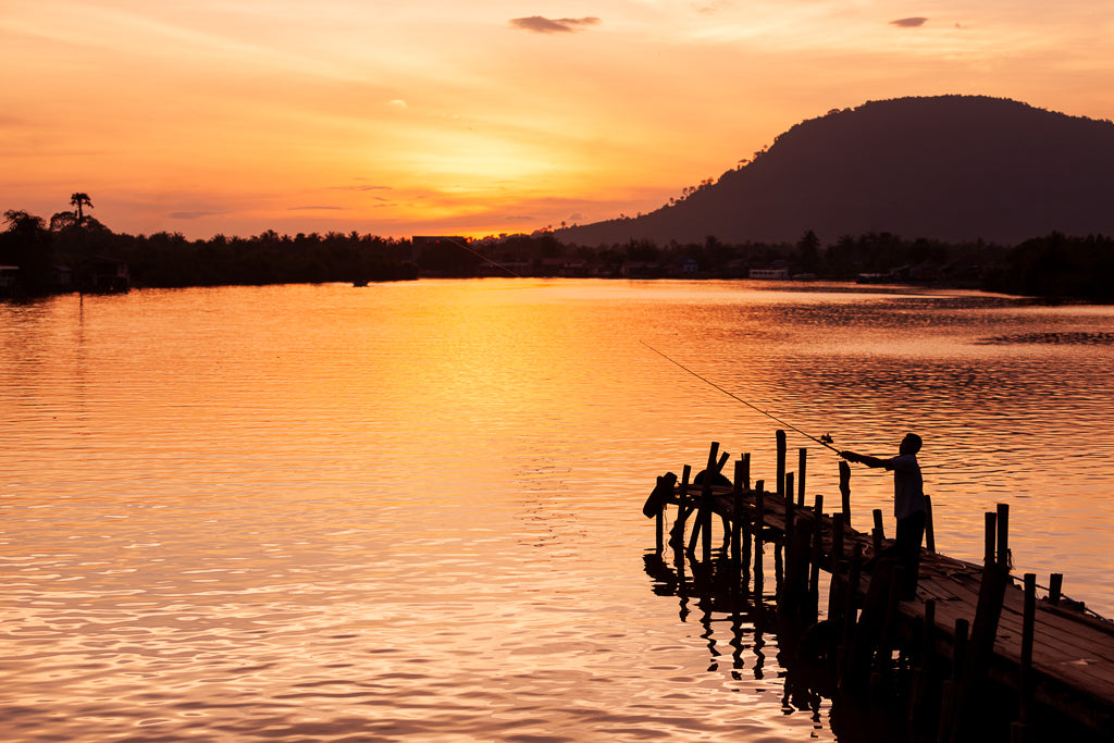 A man casting his fishing rod in to a lake in Cambodia during sunset. 