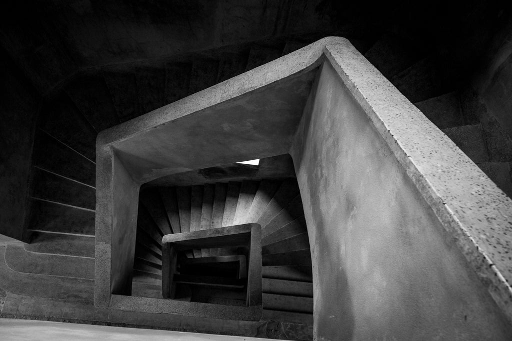 A winding stairwell with ray of light illuminating parts of it. 