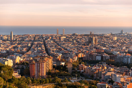 The Barcelona Sunset by FN Prints captures a breathtaking panoramic view from the Bunkers del Carmel viewpoint at dusk. This stunning print highlights the city's dense urban sprawl, with buildings stretching towards the horizon, while iconic landmarks such as the Sagrada Familia and Torre Glòries prominently stand out. In the background, you can see the serene Mediterranean Sea adding a tranquil touch to the vibrant cityscape.