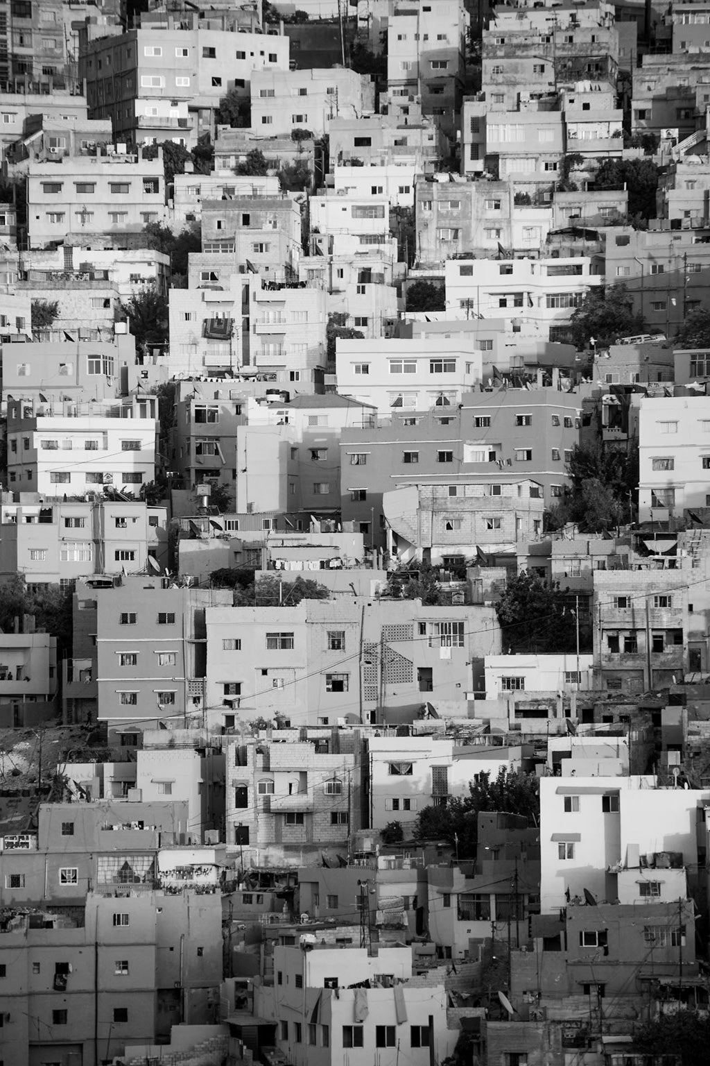 FN Prints' Jabal Amman Black & White showcases a densely packed urban neighborhood in Jabal Amman, highlighting numerous multi-story residential buildings closely situated on a hillside. The structures, varying in shape and size, are constructed with a blend of concrete and brick materials.