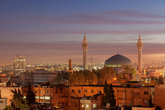 Discover the breathtaking beauty of Amman, Jordan through this exquisite piece titled "King Abdullah Mosque, Amman Jordan" by FN Prints. This stunning photograph showcases a panoramic view of the illuminated King Abdullah I Mosque, adorned with its majestic blue dome and twin minarets at twilight. The warm lights of city buildings beautifully contrast against the deepening blue and pink hues of the evening sky, capturing the essence of Amman's enchanting twilight ambiance.