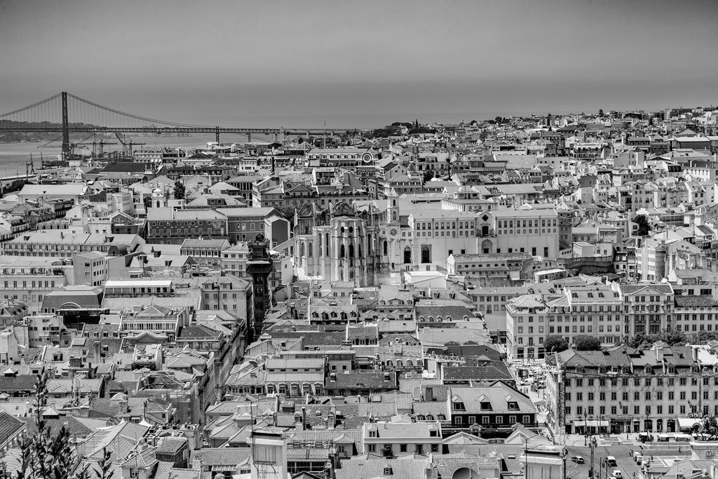 The Lisbon Cityscape print from FN Prints features a striking black and white aerial view of Lisbon, showcasing its dense historic buildings with contrasting orange rooftops. In the background, the city’s iconic 25th of April Bridge elegantly stretches across the river. The foreground is filled with rooftops and architectural details, beautifully capturing the city's timeless charm.