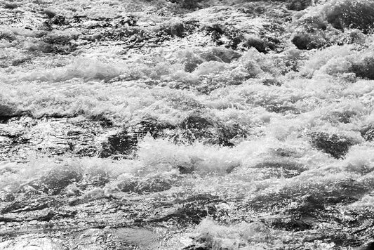 Black and white photograph titled "Whitewash" by FN Prints captures a rapidly flowing river or stream. The turbulent water, with white foam and waves crashing over rocks, creates a dynamic and energetic scene, making it perfect for Venice Beach decor.