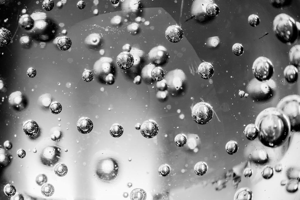 FN Prints' "Bubbles In Glass" features a striking black and white close-up of countless small bubbles suspended within a liquid medium. These bubbles, varying in size, appear to float or ascend gracefully, crafting an image of artistic sophistication against a blurred backdrop.