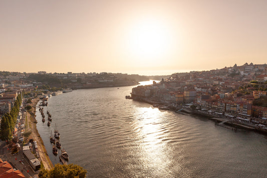 Experience the serene, sunlit view of the Douro River in Porto, Portugal with "Douro River At Sunset" by FN Prints. This stunning print captures the river bordered by historic buildings and lined with boats. Bathed in a golden sunset that casts a warm glow over the landscape, this piece of photography beautifully encapsulates Porto as it stretches out on both sides of the river.