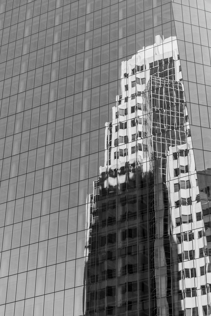 FN Prints' High Rise Reflections—a black and white photo capturing the modern glass high-rise reflecting a distorted, gridded-pattern building—showcases architectural harmony with its crisp reflection at the top that gradually warps toward the bottom.