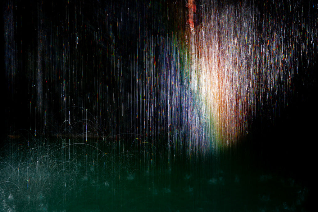 The "Spectrum" by FN Prints is a mesmerizing, vertically abstract image featuring streaks of multicolored light and a soft rainbow effect in the center against a dark background. The light patterns evoke cascading water, creating a sense of ethereal, flowing motion and a dreamy, otherworldly atmosphere akin to an ancient cave in Chouf.