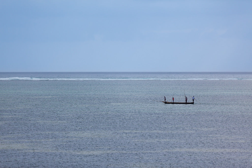 Enjoy the serene maritime adventure captured in 'The Fishermen Colour' by FN Prints, featuring a small boat with three people fishing on a calm, expansive ocean under a cloudy sky. The horizon in the background is faintly visible, elegantly separating the sky from the sea and enhancing the coastal charm of their tranquil outing.