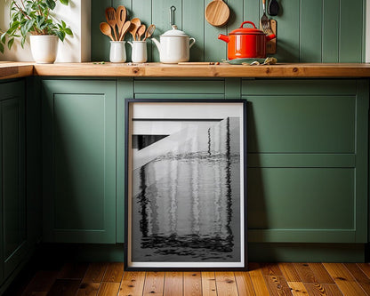 A kitchen with green cabinets and wooden countertops features minimalist decor. Cooking utensils are placed in jars, while a red pot sits on the stove. A framed piece from FN Prints, titled "Abstract Reflections," leans against the cabinet below, showcasing abstract reflections in water.