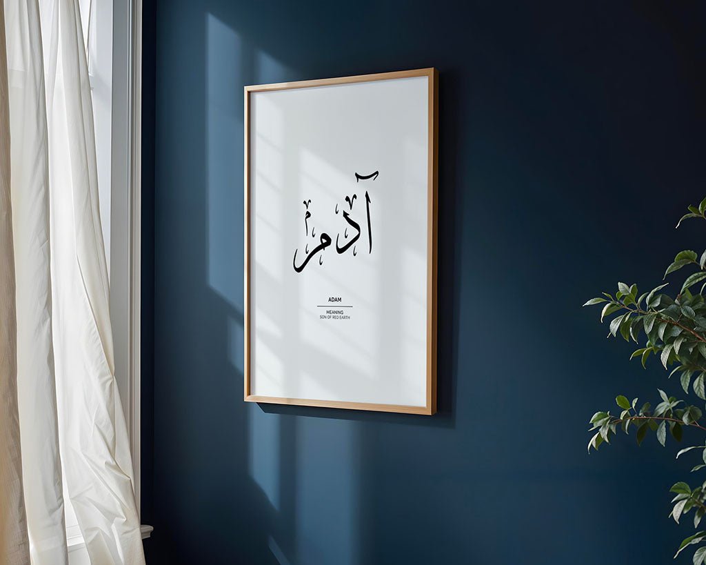 A framed "Adam - آدم" artwork by FN Prints from the Arabic Names Collection, with Arabic calligraphy and English text, hangs on a dark blue wall near a sunlit window and white curtains; a leafy green plant is in the lower right corner.