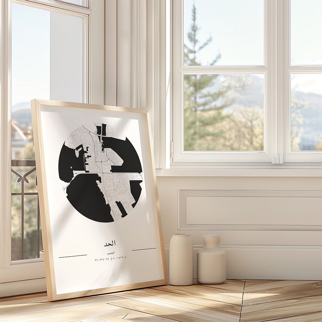 The FN Prints Al Hidd City Map, a framed minimalist print featuring Arabic text, rests on the floor of a bright room with light walls and beige vases, creating serene Bahrain wall art with window views of trees and mountains.