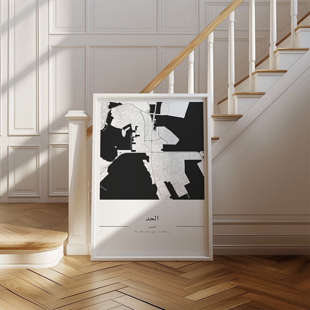 The Al Hidd City Map by FN Prints, a framed minimalist print, rests on the floor against a staircase with wooden steps and white railings in a bright modern room with paneled walls and herringbone wood floors.