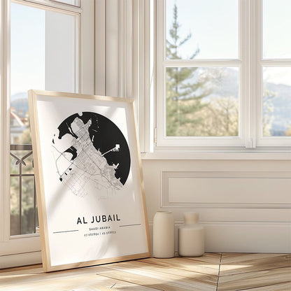 The FN Prints "Al Jubail City Map" minimalist framed print rests against a wall by a sunny window, with two decorative vases beside it on the wooden floor.