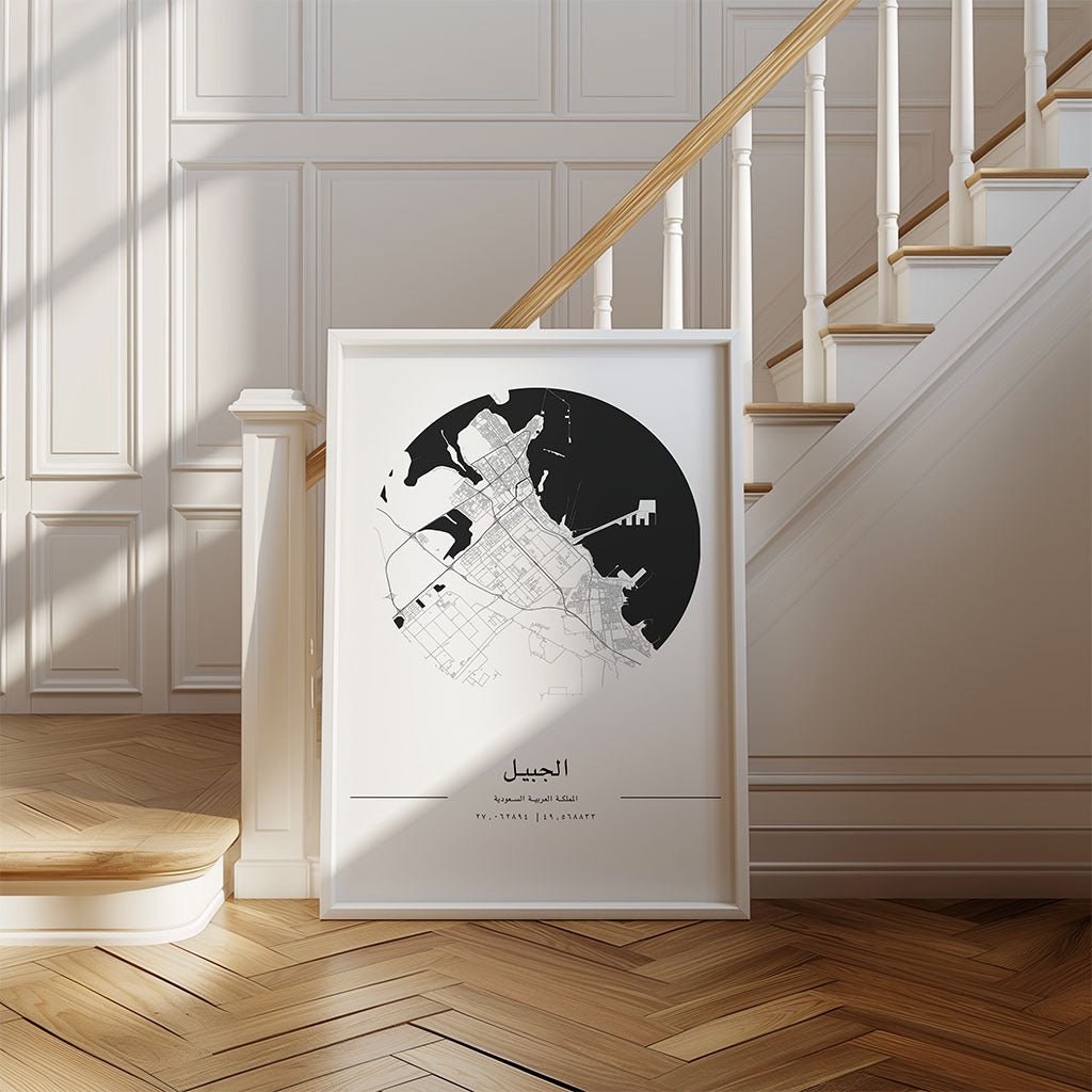 The FN Prints Al Jubail City Map, featuring Arabic text, sits on a wood floor by a staircase with white trim and wooden handrail, adding Saudi Arabian charm to a bright interior.