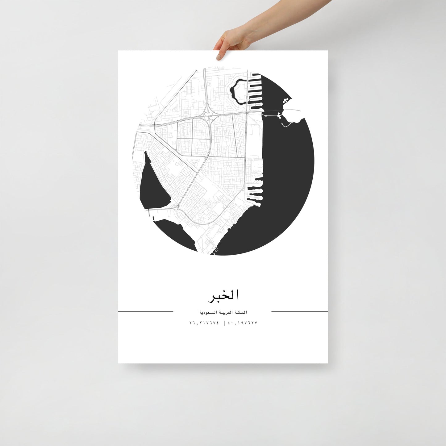 A hand holding a black and white map poster of Al Khobar city, with distinct areas marked in white on a black background.