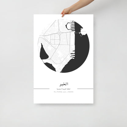 A hand holding a black and white map poster of Al Khobar city, with distinct areas marked in white on a black background.