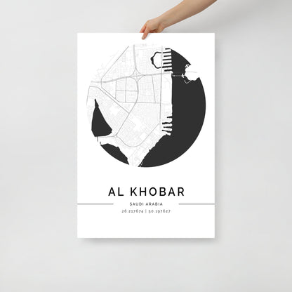 A hand holding a black and white map poster of Al Khobar city, with distinct areas marked in white on a black background.