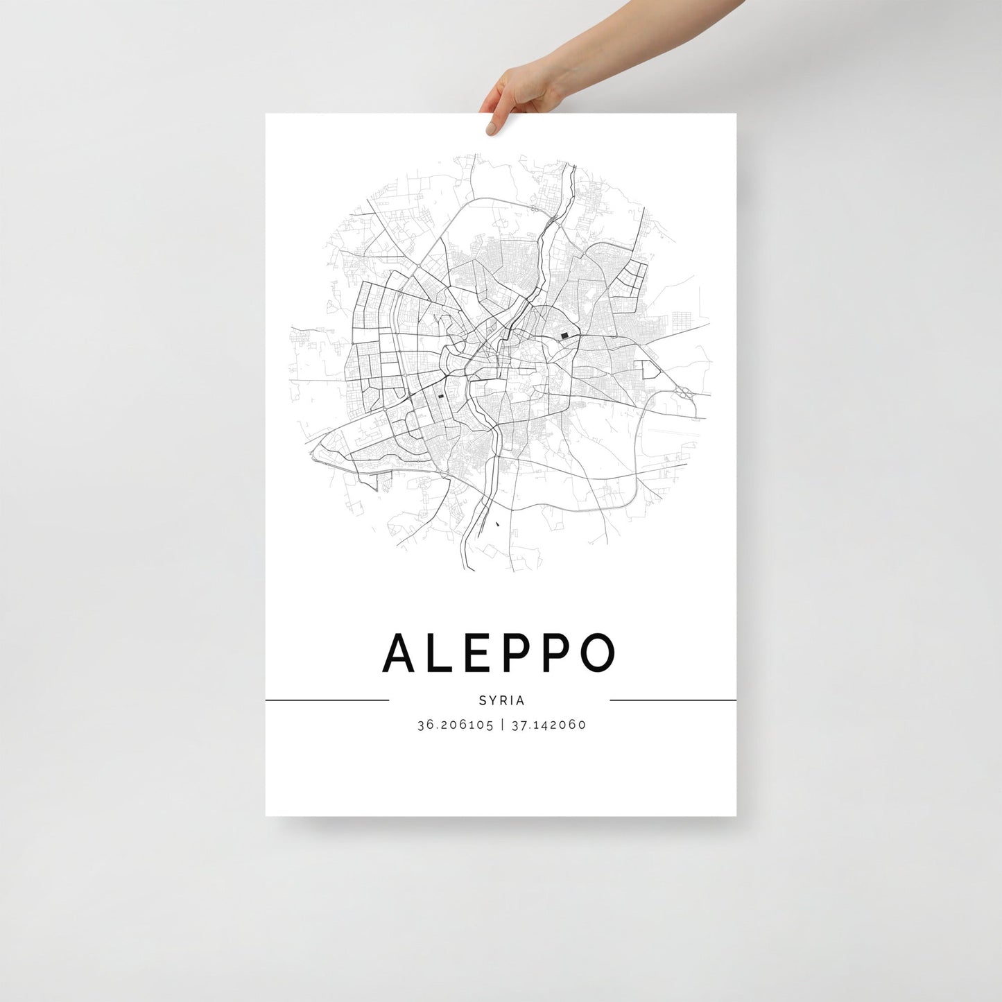 A person holds the minimalist black and white Aleppo Map from FN Prints, showcasing a detailed street map. This sophisticated wall art print features coordinates 36.206105 | 37.142060, capturing Aleppo's charm in a sleek design.
